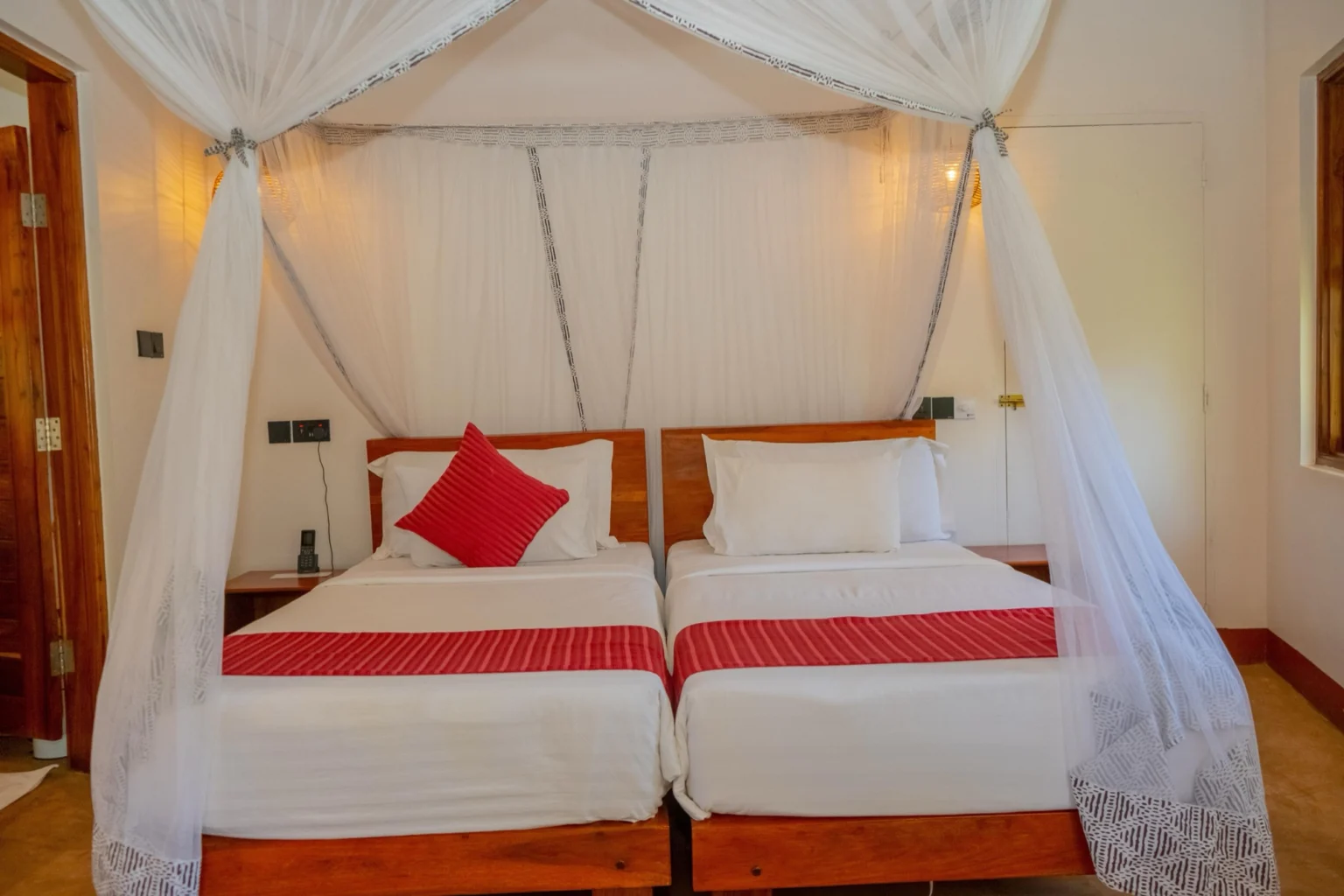 Twin beds with red runners under a canopy mosquito net