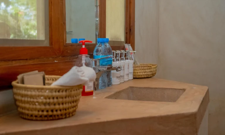 Bathroom vanity with Ikumbi toiletries, bottled water and woven baskets beside a polished concrete basin